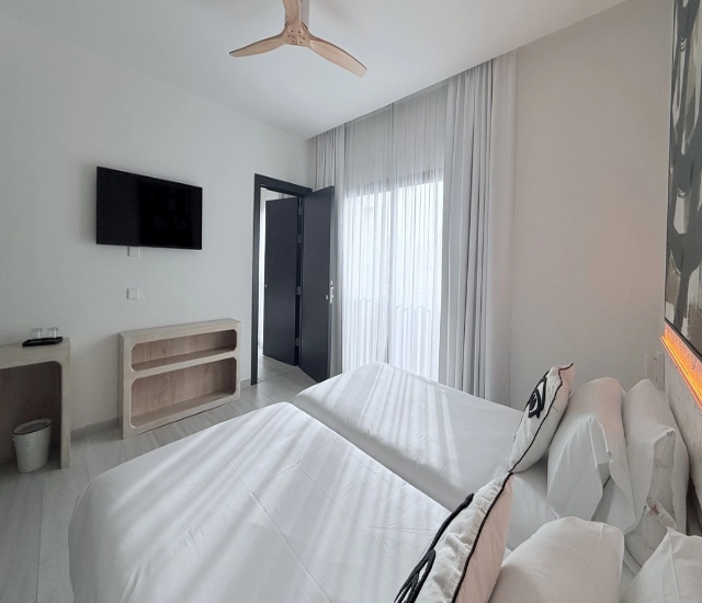 Habitaci&oacute;n moderna con dos camas, televisor y ventilador de techo.