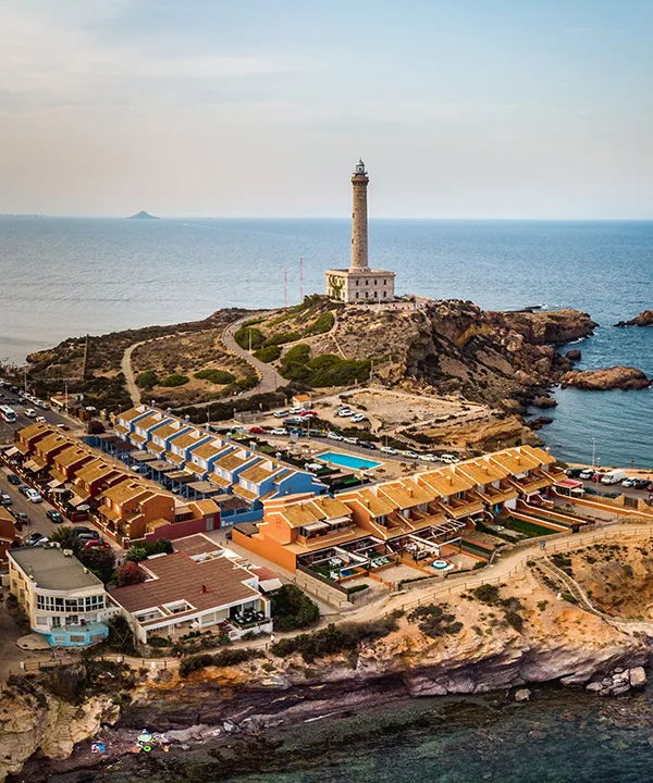 Vista a&eacute;rea de un faro junto al mar y casas cercanas en la costa.