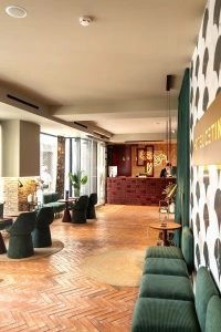 Vestíbulo moderno de hotel con sofás verdes y mostrador de recepción al fondo.
