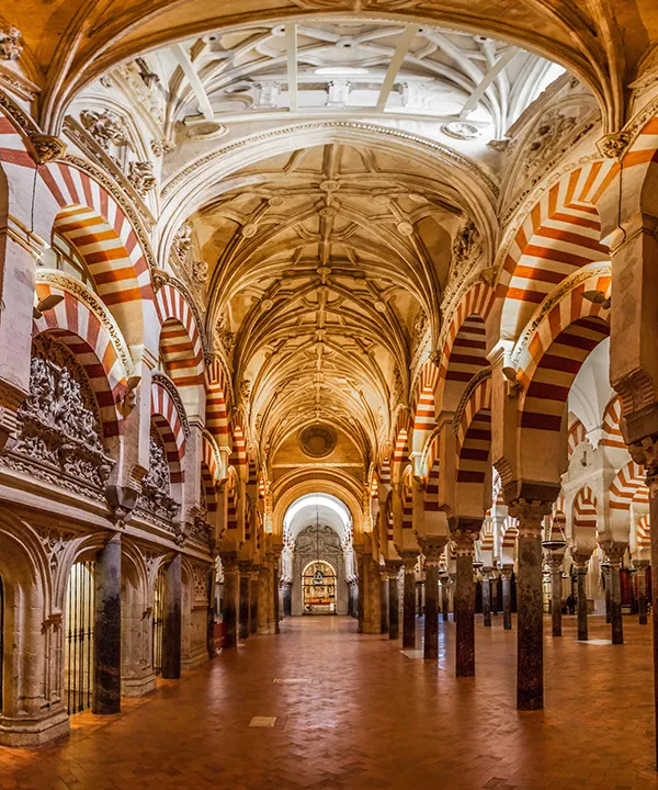 Interior de una mezquita con arcos de rayas y un techo detallado.