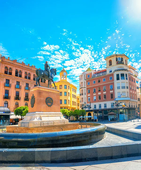 Plaza con estatua ecuestre y edificios coloridos bajo un cielo azul.