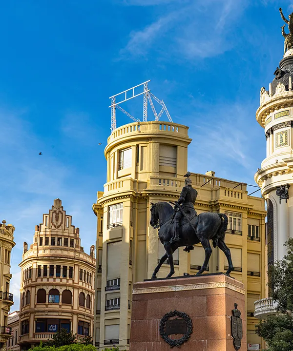 Estatua ecuestre frente a edificios antiguos con cielo azul.