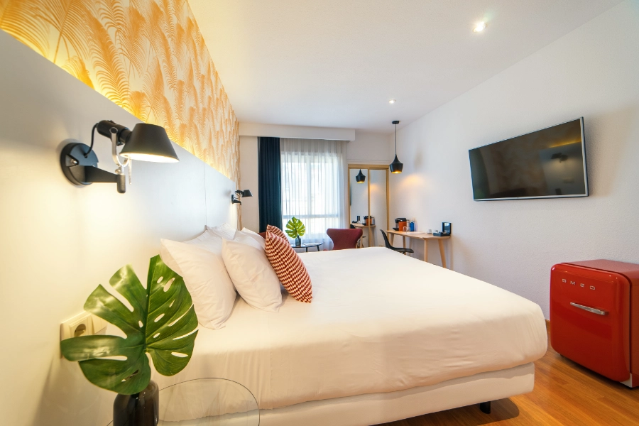 Habitación moderna con cama doble, TV y mini-nevera roja.