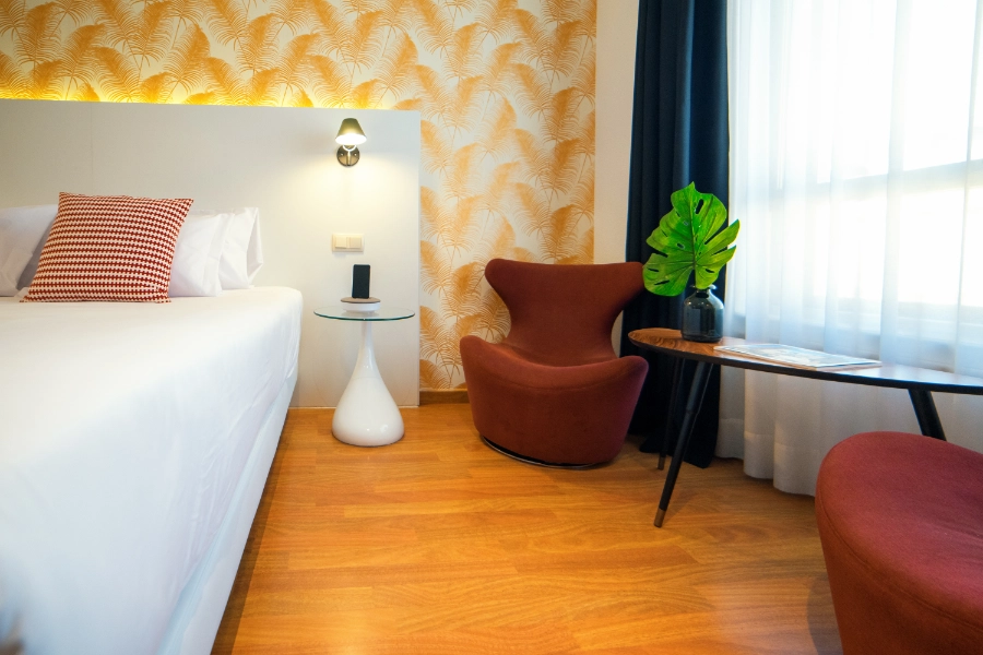 Habitación moderna con silla roja, mesa, y planta junto a una ventana iluminada.