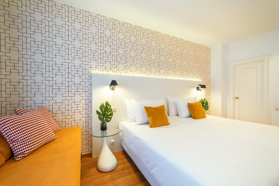 Habitación moderna con cama doble, cojines naranjas y decoración geométrica.
