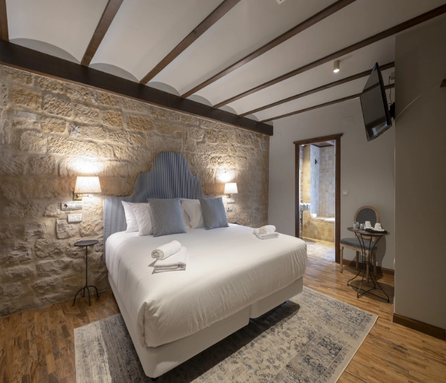 Habitaci&oacute;n con cama doble, decorada con paredes de piedra y vigas de madera.