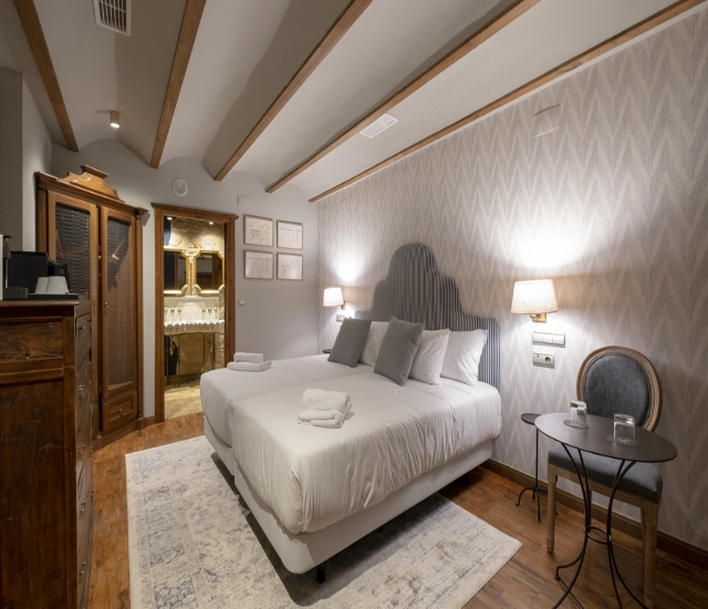 Habitaci&oacute;n elegante con cama doble, l&aacute;mparas, alfombra y muebles de madera.