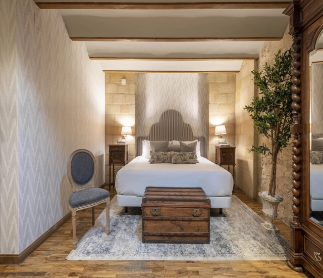 Habitaci&oacute;n con cama, ba&uacute;l, silla y armario, decorada en estilo cl&aacute;sico.