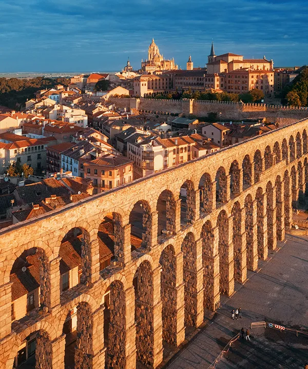 Acueducto romano al atardecer con catedral al fondo en una ciudad hist&oacute;rica.