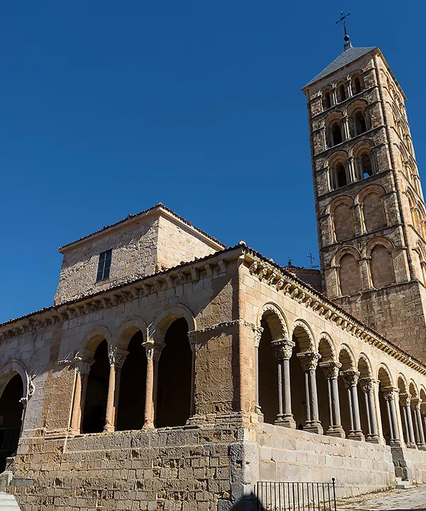 Iglesia medieval con torre alta y arcos, bajo un cielo azul claro.