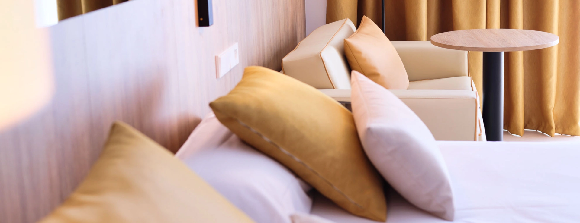 Cama con cojines amarillos junto a un sill&oacute;n y una mesa redonda.