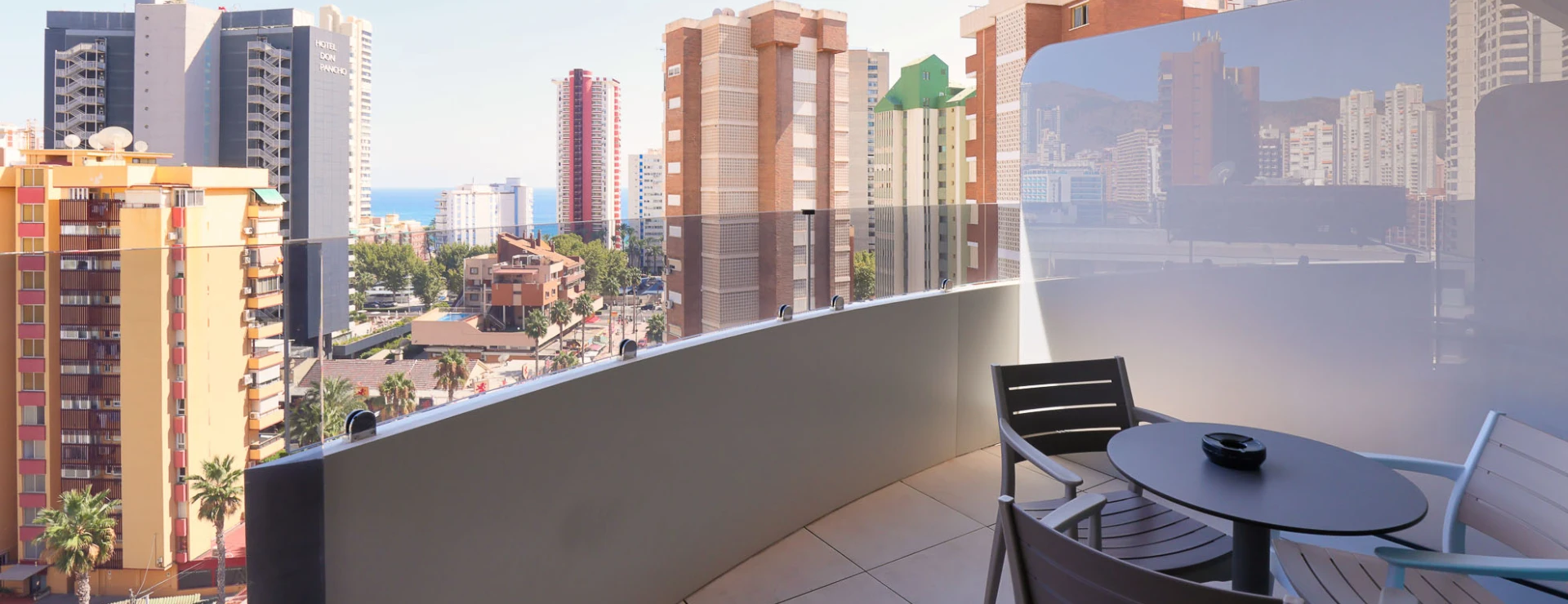 Balc&oacute;n con muebles, vista urbana y edificios al fondo.