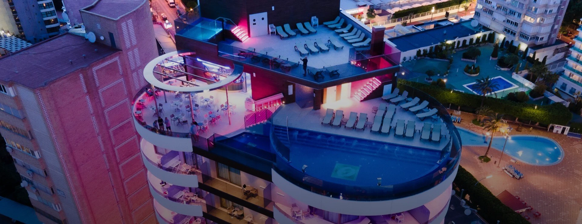 Techo de edificio con piscina y bar iluminado en la noche.