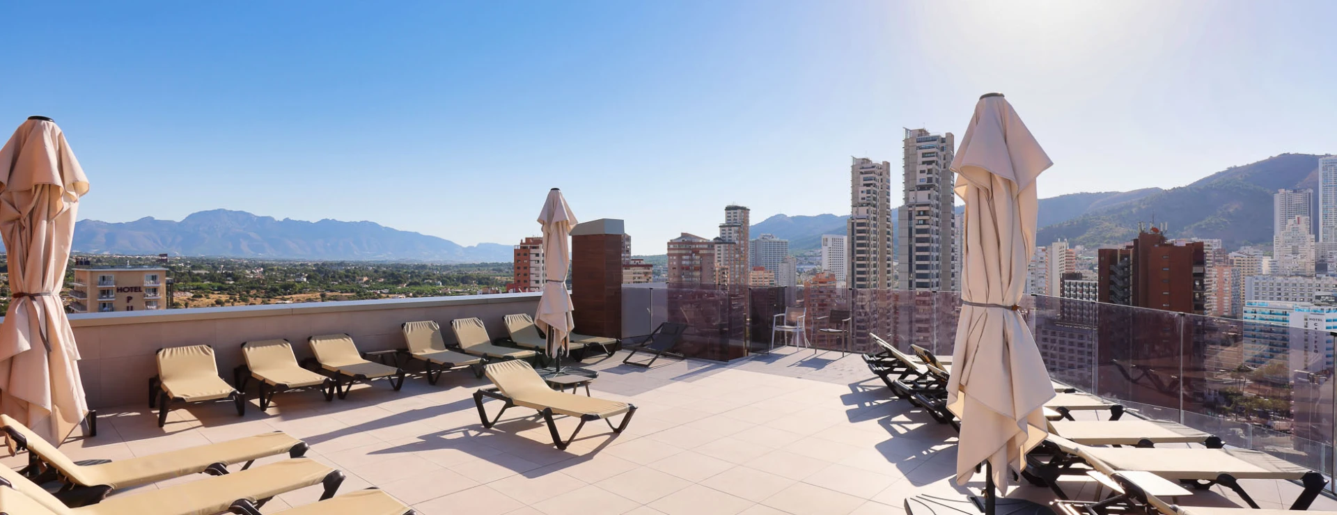 Terraza con tumbonas, sombrillas y vista a la ciudad y monta&ntilde;a.
