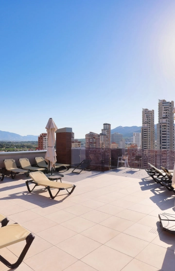 Terraza con tumbonas, sombrillas y vista urbana bajo un cielo despejado.