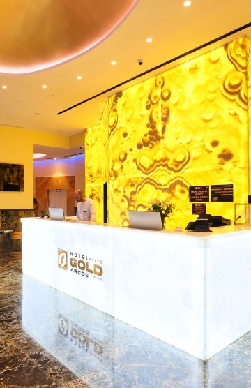 Recepci&oacute;n moderna de hotel con fondo dorado iluminado.