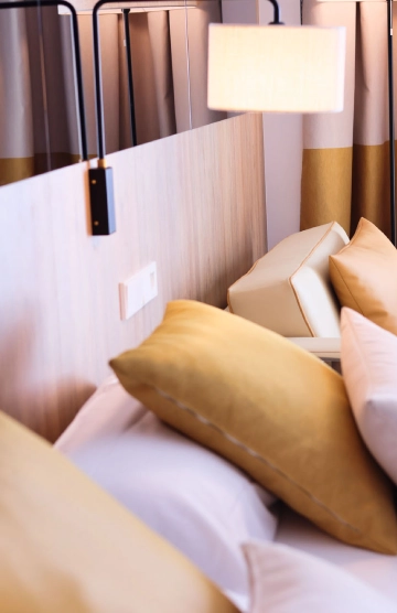 Cama con cojines dorados y l&aacute;mpara colgante en habitaci&oacute;n moderna.