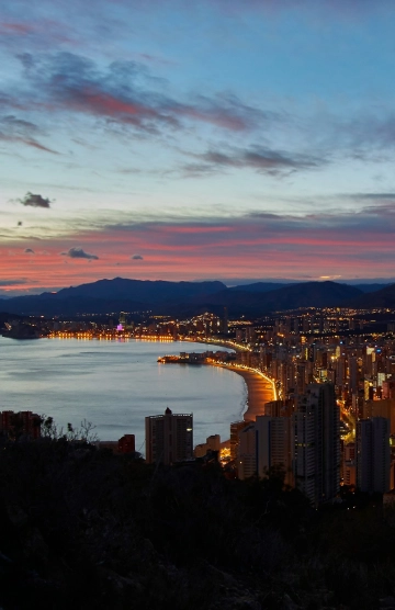 Vista nocturna de una ciudad costera iluminada al atardecer.
