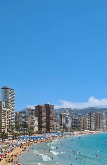 Playa abarrotada con edificios altos y cielo despejado.