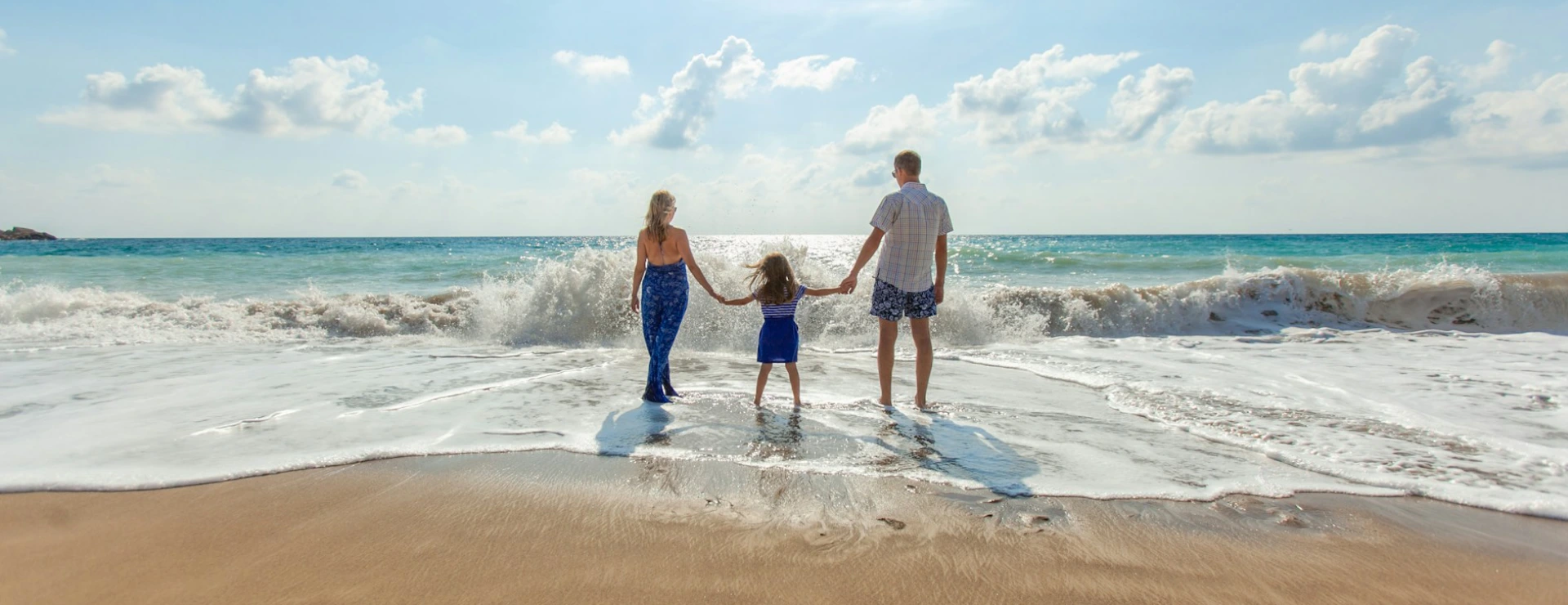 Familia de tres en la playa mirando al mar bajo un cielo despejado.