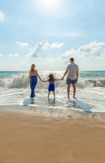 Familia de tres en la playa, caminando hacia el mar tomados de la mano.