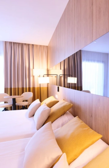 Cama con cojines dorados, espejo y l&aacute;mpara en habitaci&oacute;n moderna.