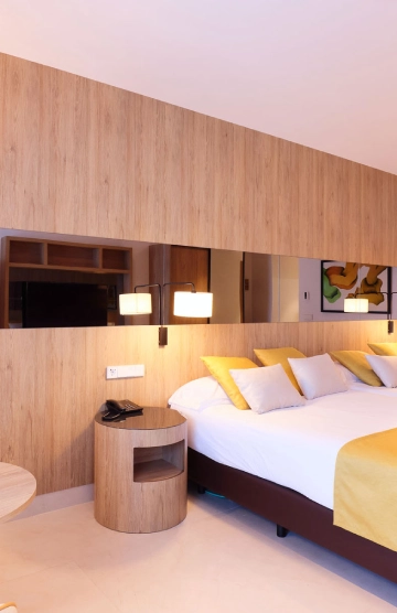 Habitaci&oacute;n moderna con cama, cojines amarillos y l&aacute;mparas de pared.