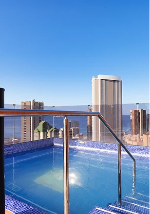 Piscina en azotea con vista a la ciudad y edificios altos al fondo.