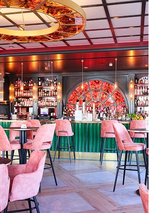 Bar elegante con taburetes rosados y botellas en estantes iluminados.