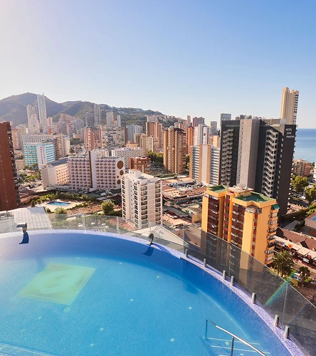 Piscina infinita con vista a una ciudad costera con edificios altos.