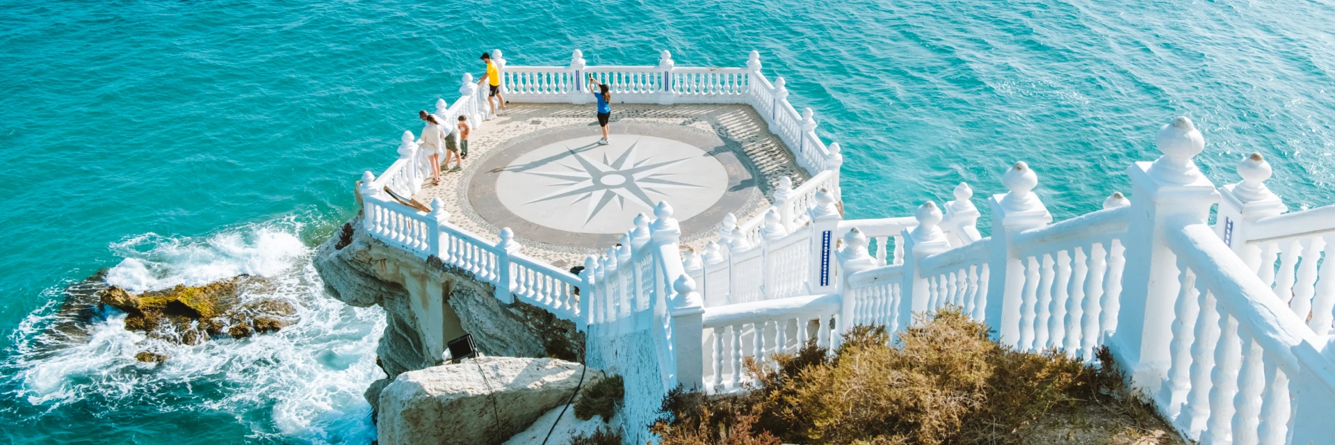 Mirador costero con barandilla blanca sobre el mar azul claro.
