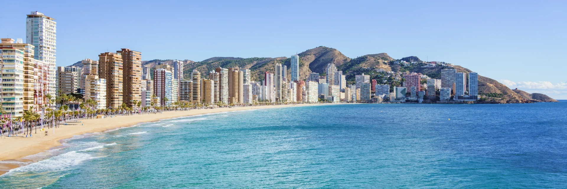 Playa con edificios altos y monta&ntilde;as al fondo.