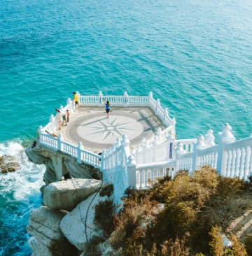 Mirador con barandillas blancas sobre un acantilado frente al mar azul cristalino.