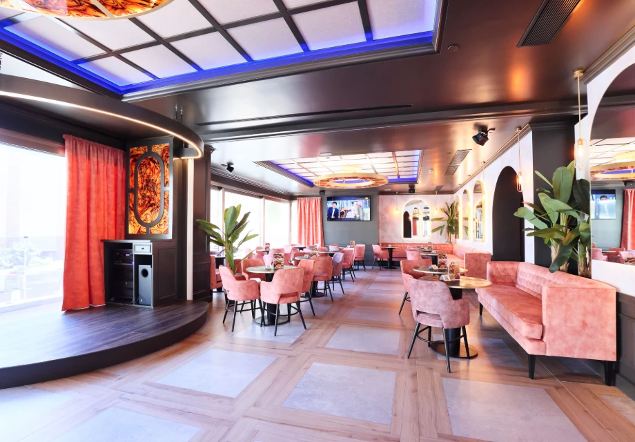 Restaurante moderno con sillas rosas, cortinas y plantas decorativas.