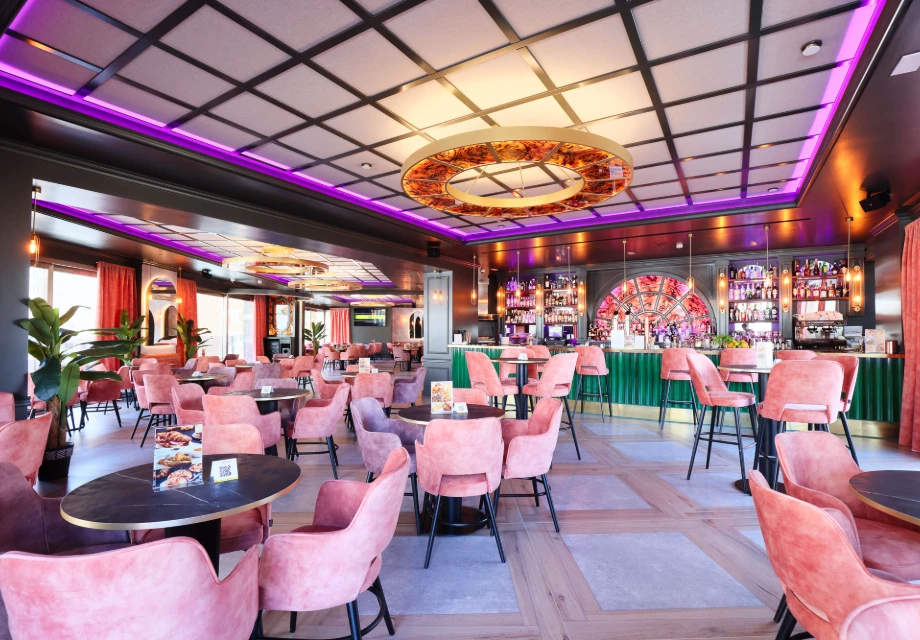 Moderno restaurante con sillas rosadas, decoraci&oacute;n colorida y barra al fondo.
