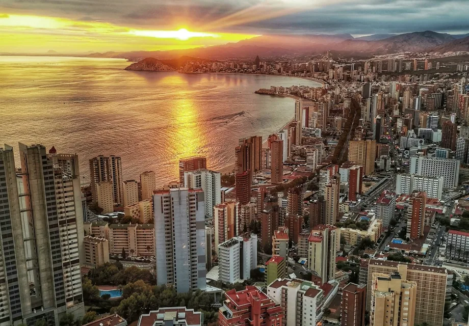 Amanecer sobre la ciudad costera con muchos edificios y el mar reflejando el sol.