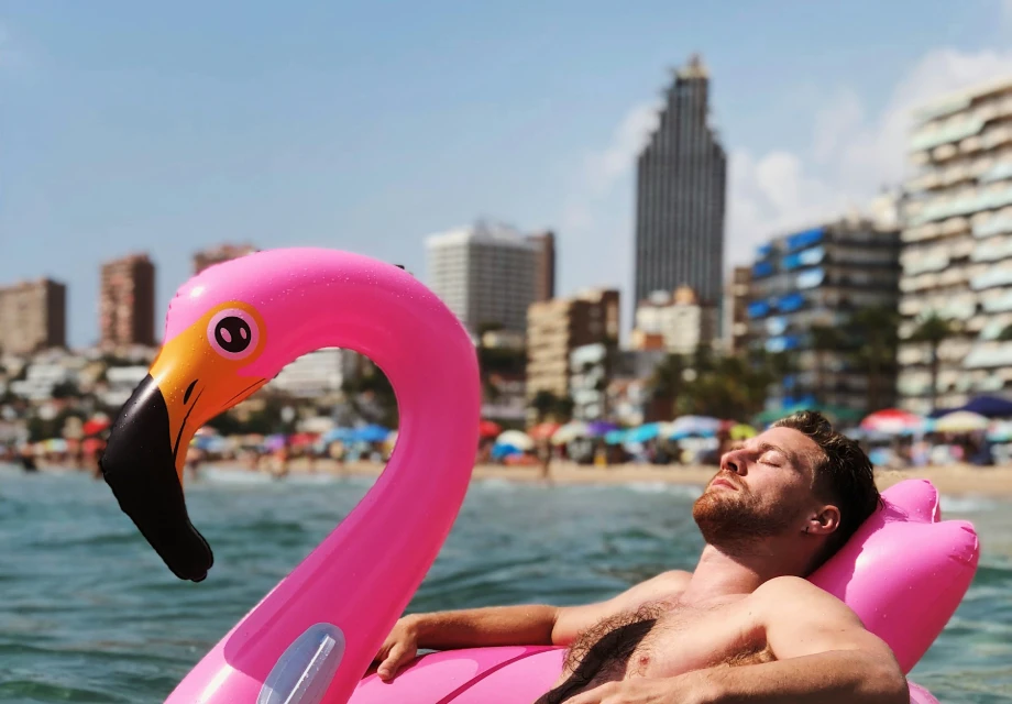 Hombre relaj&aacute;ndose en flotador de flamenco rosa en la playa.