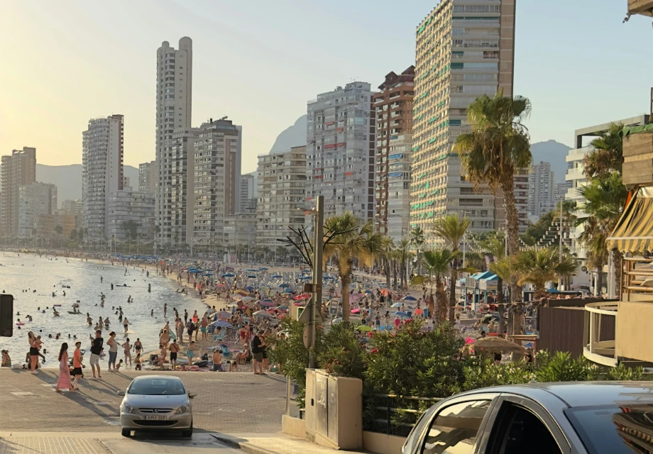 Playa concurrida con edificios altos al fondo y palmeras a la orilla del mar.