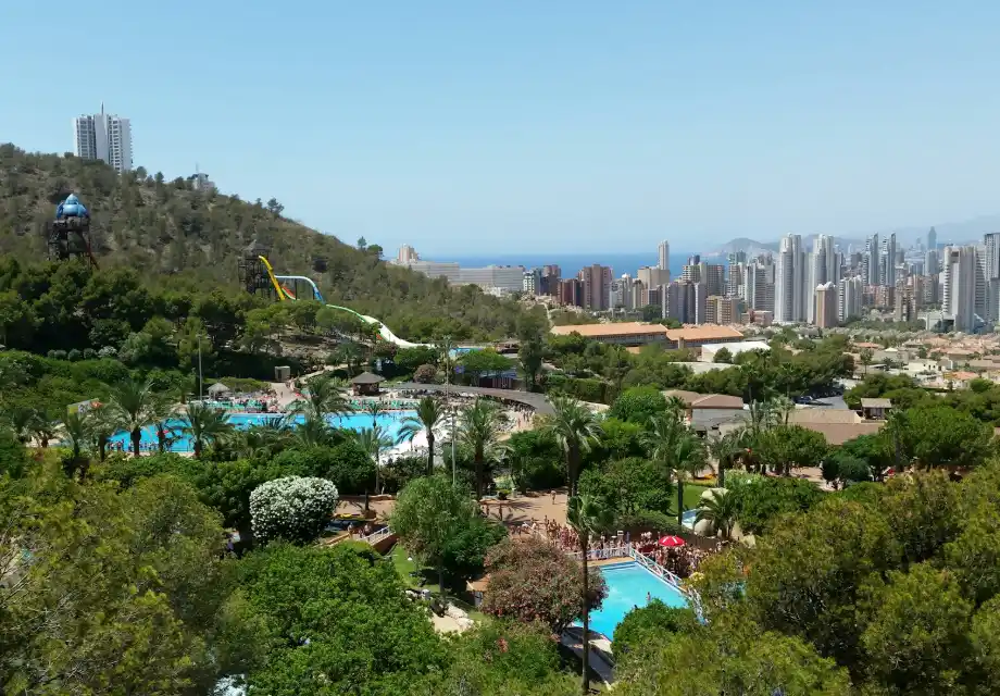 Parque acu&aacute;tico con piscinas, toboganes y ciudad al fondo.