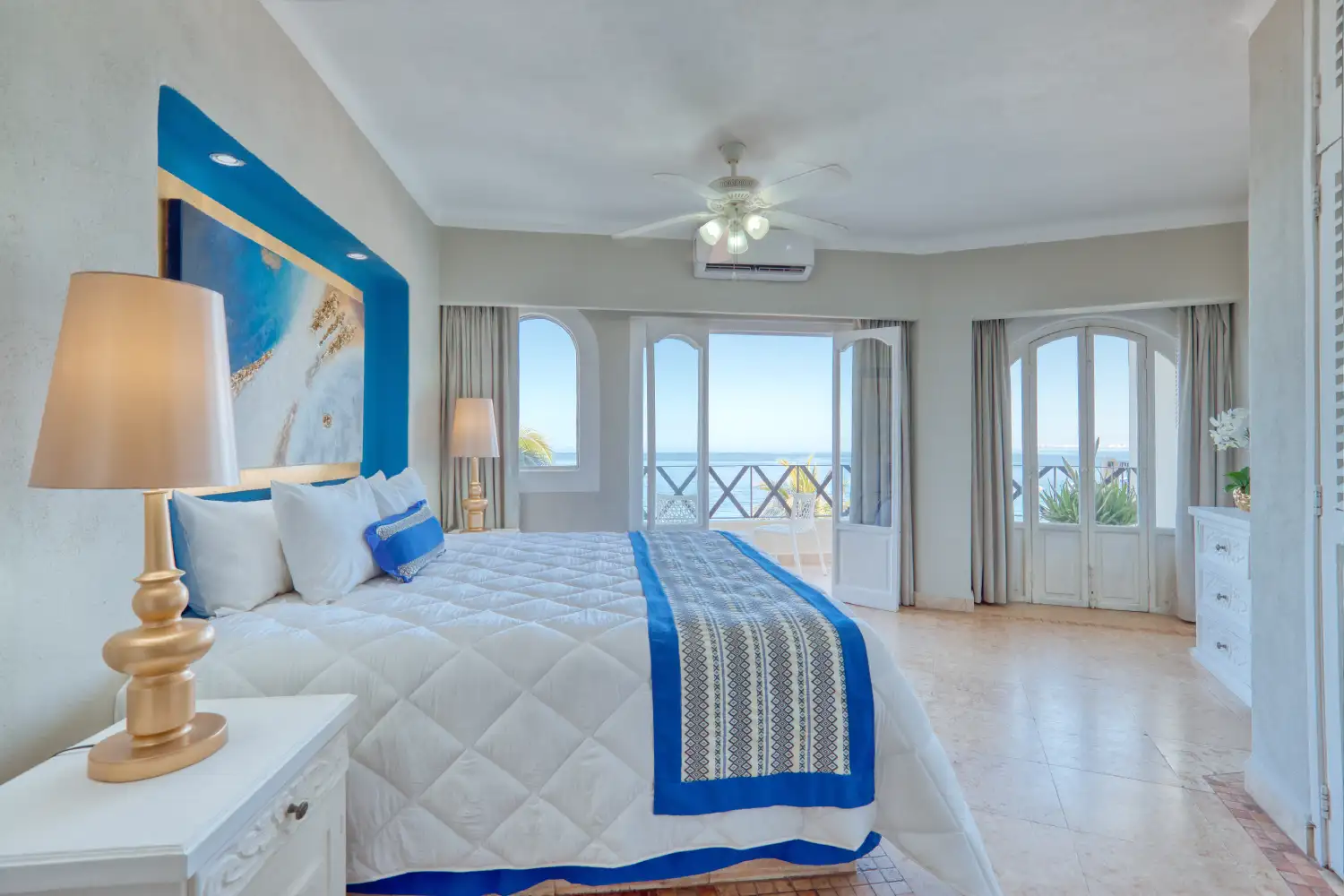 Habitaci&oacute;n luminosa con cama grande, decoraci&oacute;n azul y vista al mar.