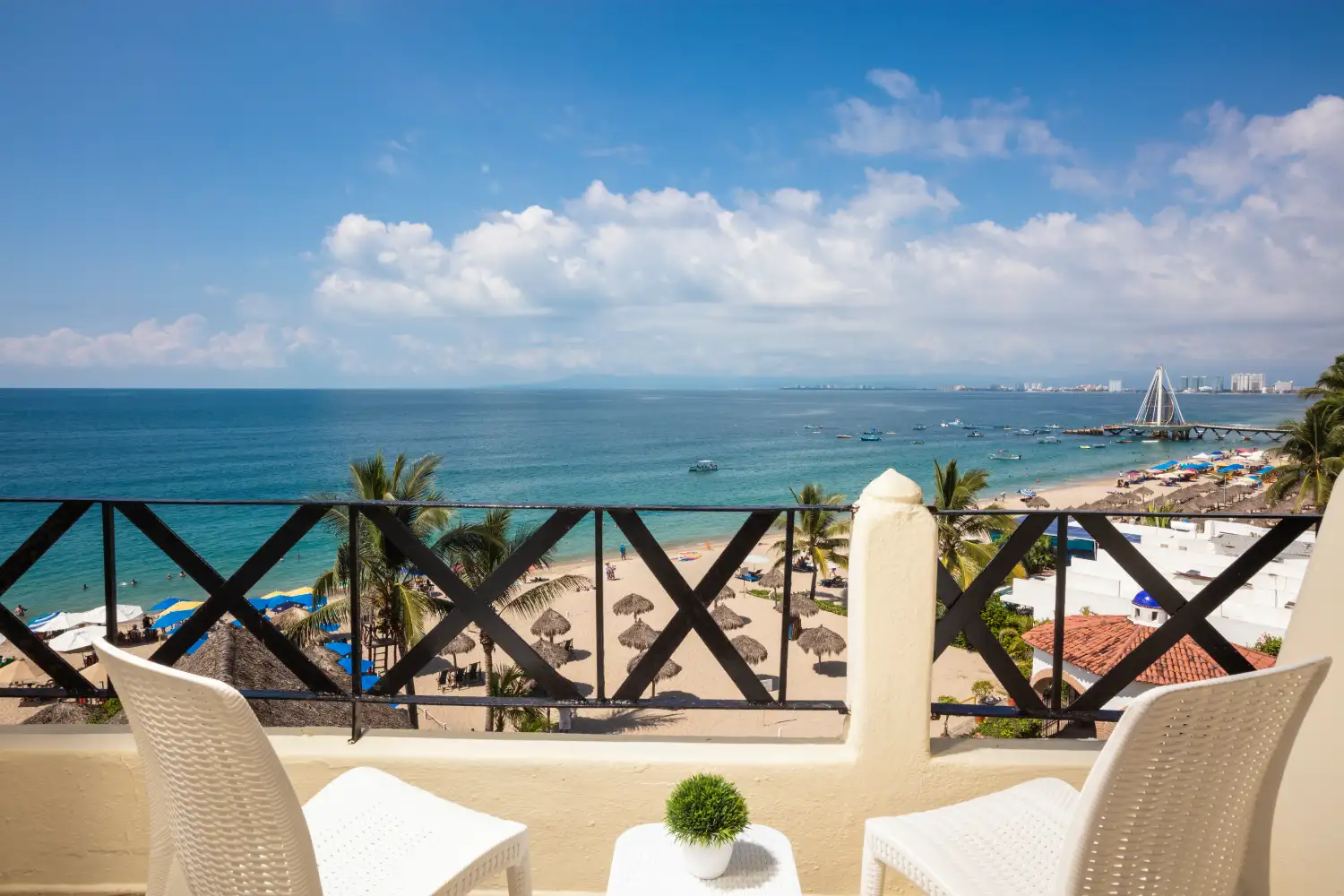 Vista al mar desde un balc&oacute;n con sillas blancas y sombrillas en la playa.