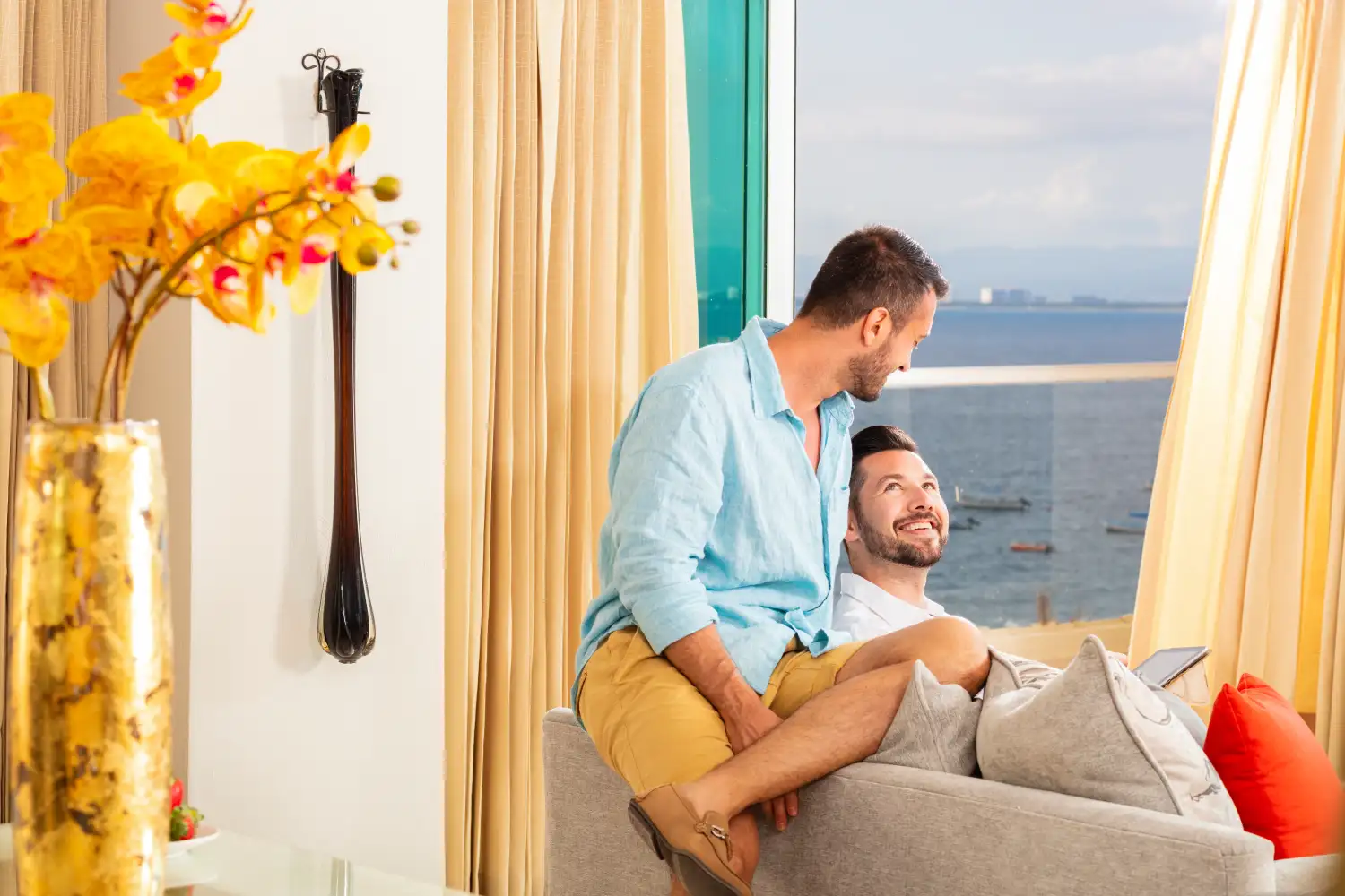 Pareja sonriendo frente al mar, con flores amarillas a un lado.