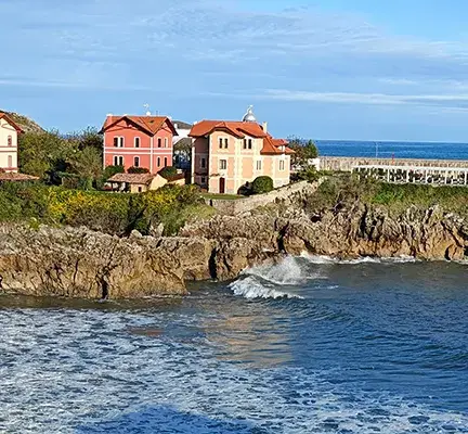 Casas junto al acantilado con vistas al mar. Cielo despejado y olas suaves.