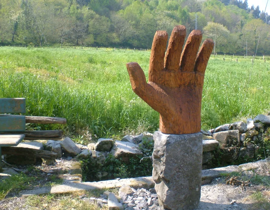 Escultura de mano de metal oxidado en un jard&iacute;n, con pasto y piedras.