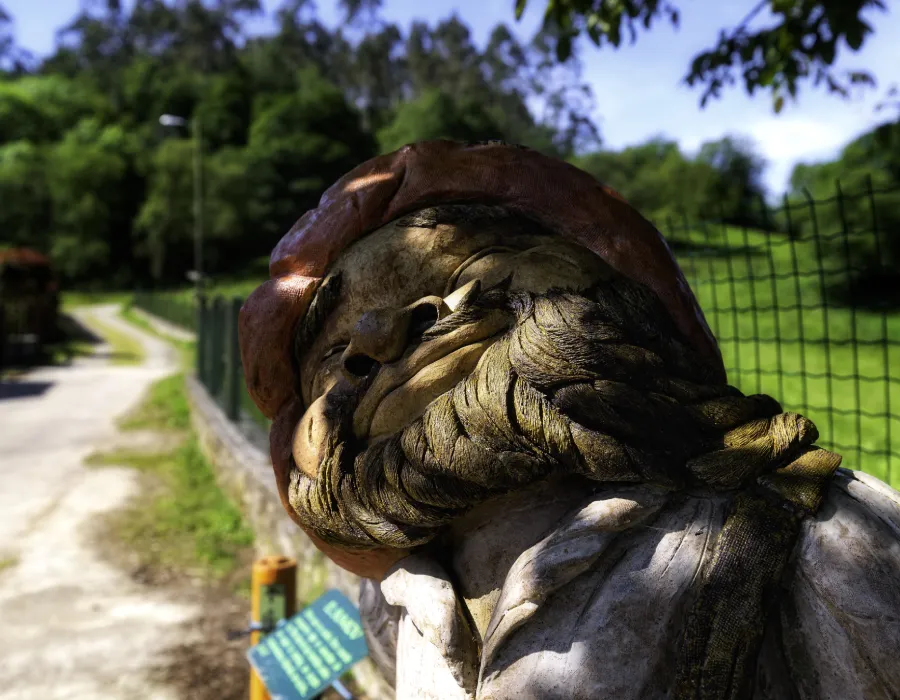 Escultura de bronce de un hombre, con jard&iacute;n y camino al fondo.