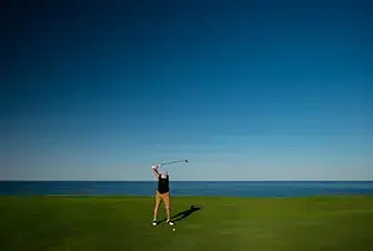 Persona jugando golf en un campo junto al mar bajo un cielo despejado.
