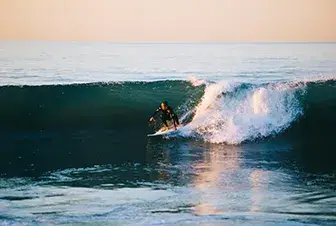 Persona surfeando una ola grande al atardecer en el oc&eacute;ano.