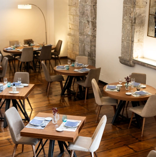 Restaurante elegante con mesas de madera y sillas beige sobre piso de madera.