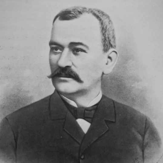 Un hombre con bigote en una foto en blanco y negro, vistiendo traje formal.