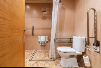 Ba&ntilde;o accesible con ducha, inodoro, barandales y puerta de madera.